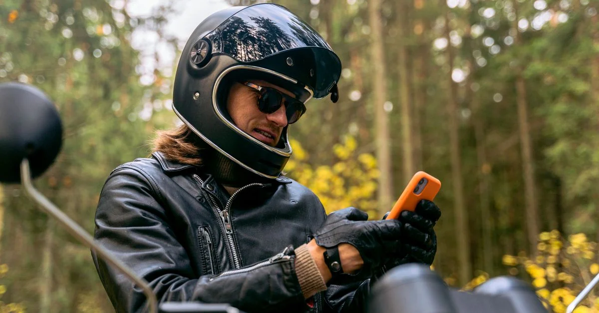 Un motard en tenue de protection consulte son smartphone pendant qu'il est garé dans une forêt.